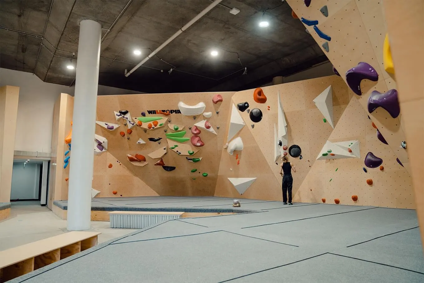 Interior of NOMAD Bouldering Gym with colourful climbing walls and active climbers.